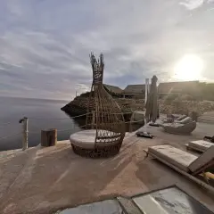 Terrasse en bord de mer à Dakhla, Maroc, avec des chaises longues, un fauteuil en rotin et des bâtiments au toit de chaume.