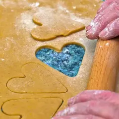 Des mains saupoudrées de farine utilisent un rouleau à pâtisserie pour découper des cœurs dans la pâte, comme des jeux de mémoire pour la Saint-Valentin.