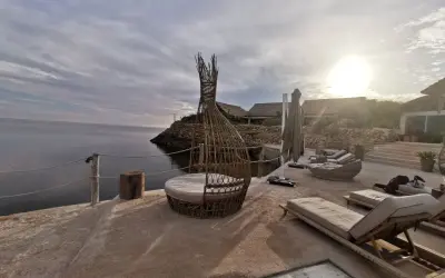 Terrasse en bord de mer à Dakhla, Maroc, avec des chaises longues, un fauteuil en rotin et des bâtiments au toit de chaume.
