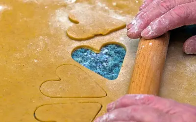 Des mains saupoudrées de farine utilisent un rouleau à pâtisserie pour découper des cœurs dans la pâte, comme des jeux de mémoire pour la Saint-Valentin.