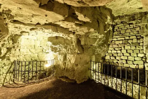 Intérieur des boves d'Arras, un réseau de galeries souterraines aux murs de pierre brute et de briques, éclairées par une lumière jaune.
