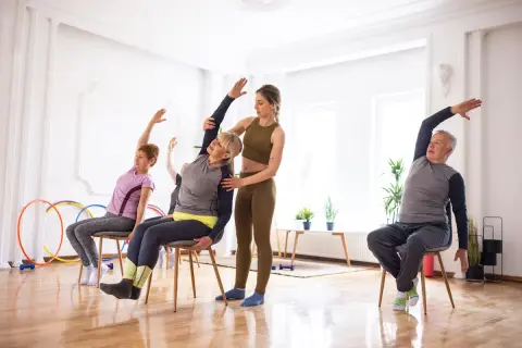 Cours de gym avec une chaise : une monitrice guide des seniors dans des étirements doux.