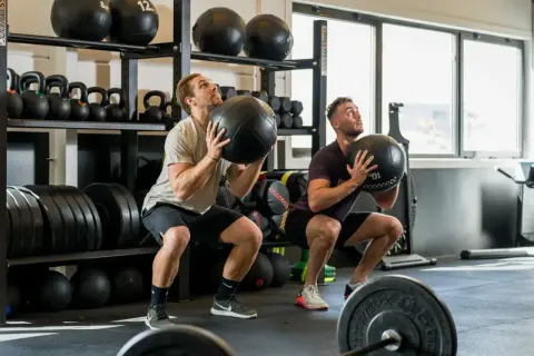 Deux hommes font des squats avec des medecine balls. Un bon sport pour maigrir et se muscler.