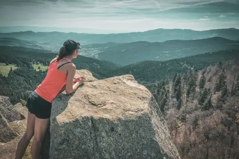 Une femme profite d'une vue panoramique sur les Vosges lors d'un trek. Les montagnes s'étendent à perte de vue sous un ciel nuageux.