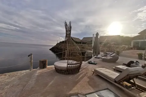 Terrasse en bord de mer à Dakhla, Maroc, avec des chaises longues, un fauteuil en rotin et des bâtiments au toit de chaume.