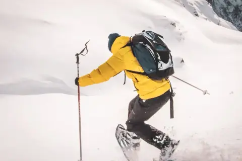 Person en raquettes, veste jaune vif, explorant un paysage enneigé. Les bâtons de randonnée aident à progresser dans la poudreuse.