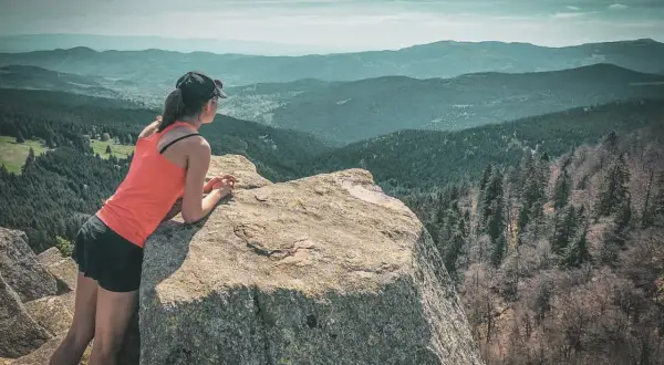 Une randonneuse admire le paysage depuis un rocher. Une parfaite destination randonnée pour s'évader.