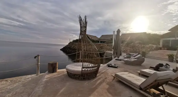 Terrasse en bord de mer à Dakhla, Maroc, avec des chaises longues, un fauteuil en rotin et des bâtiments au toit de chaume.