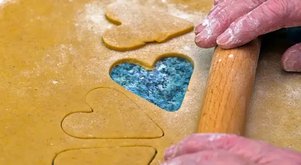 Des mains saupoudrées de farine utilisent un rouleau à pâtisserie pour découper des cœurs dans la pâte, comme des jeux de mémoire pour la Saint-Valentin.