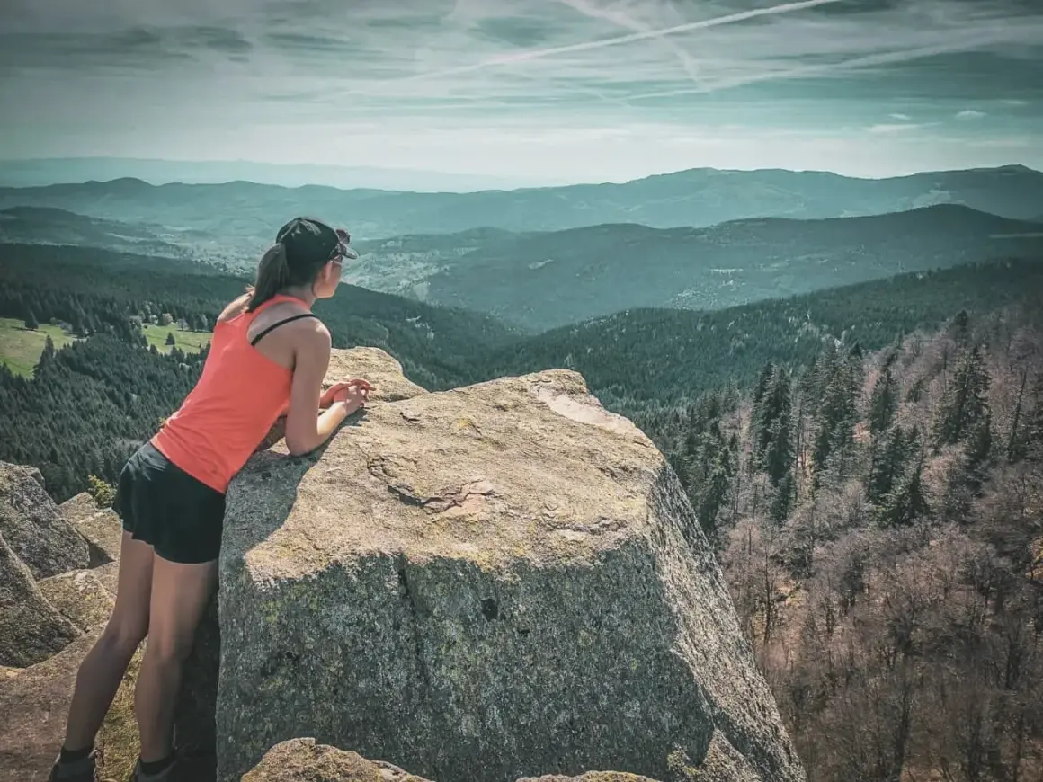 Une randonneuse admire le paysage depuis un rocher. Une parfaite destination randonnée pour s'évader.