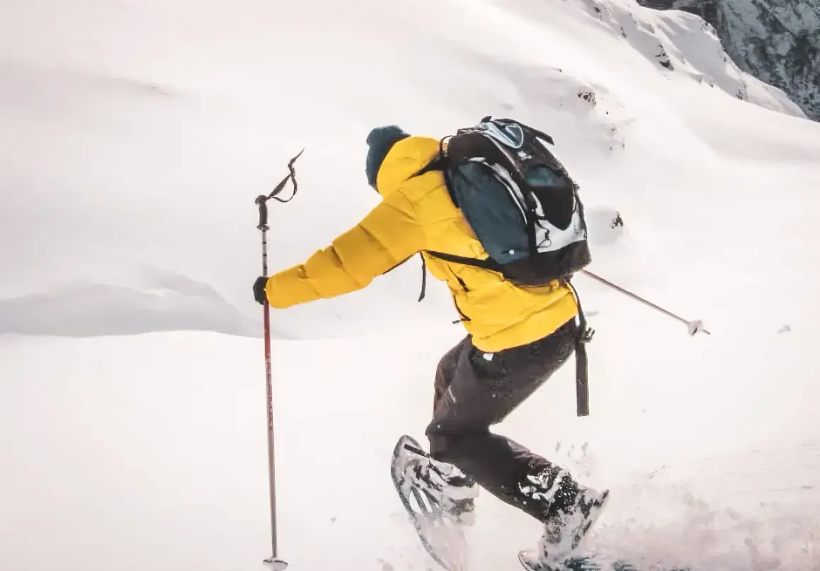 Person en raquettes, veste jaune vif, explorant un paysage enneigé. Les bâtons de randonnée aident à progresser dans la poudreuse.