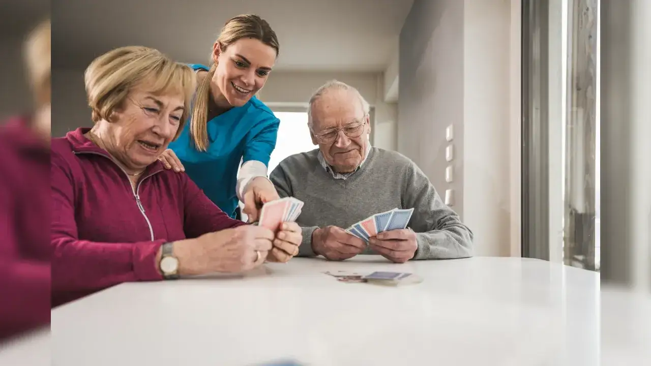 Une aide-soignante encourage des personnes âgées à jouer aux cartes, stimulant ainsi leurs exercices orthophoniques et leur mémoire.