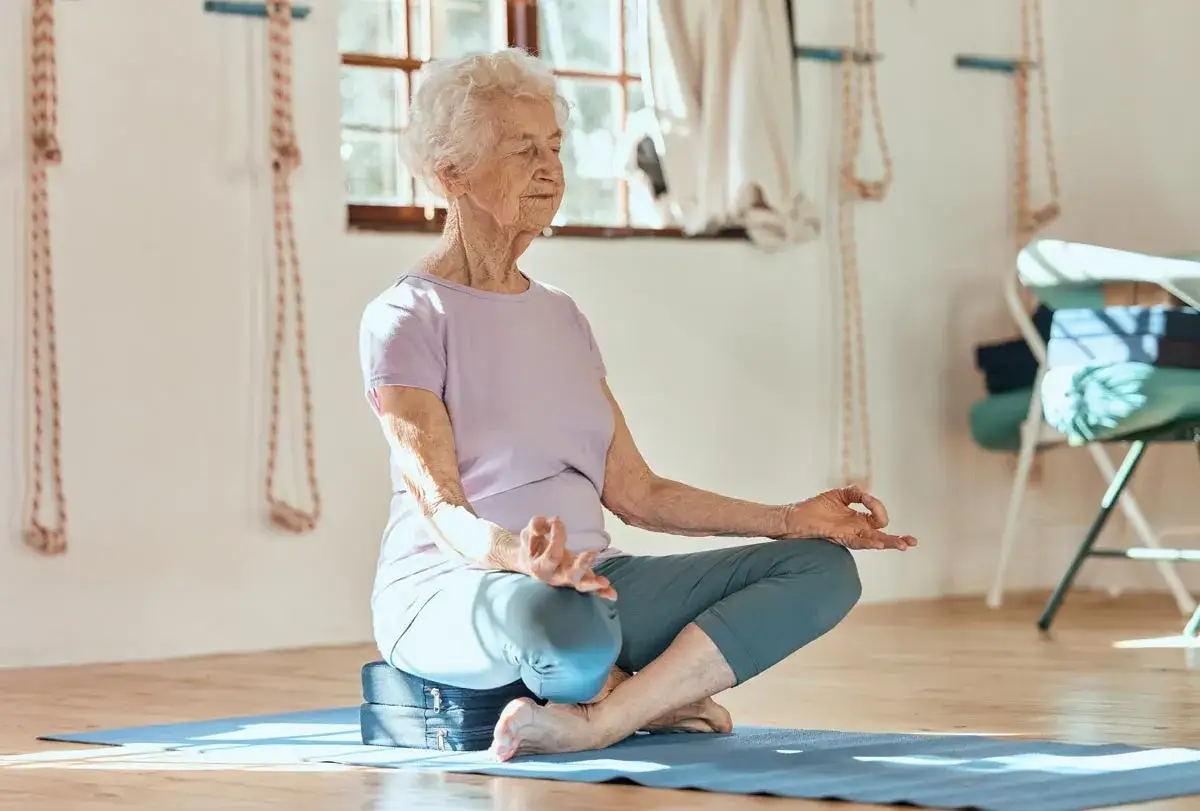 Une femme âgée médite, les yeux fermés, dans une salle de yoga. Une pratique bénéfique pour la stimulation cognitive.