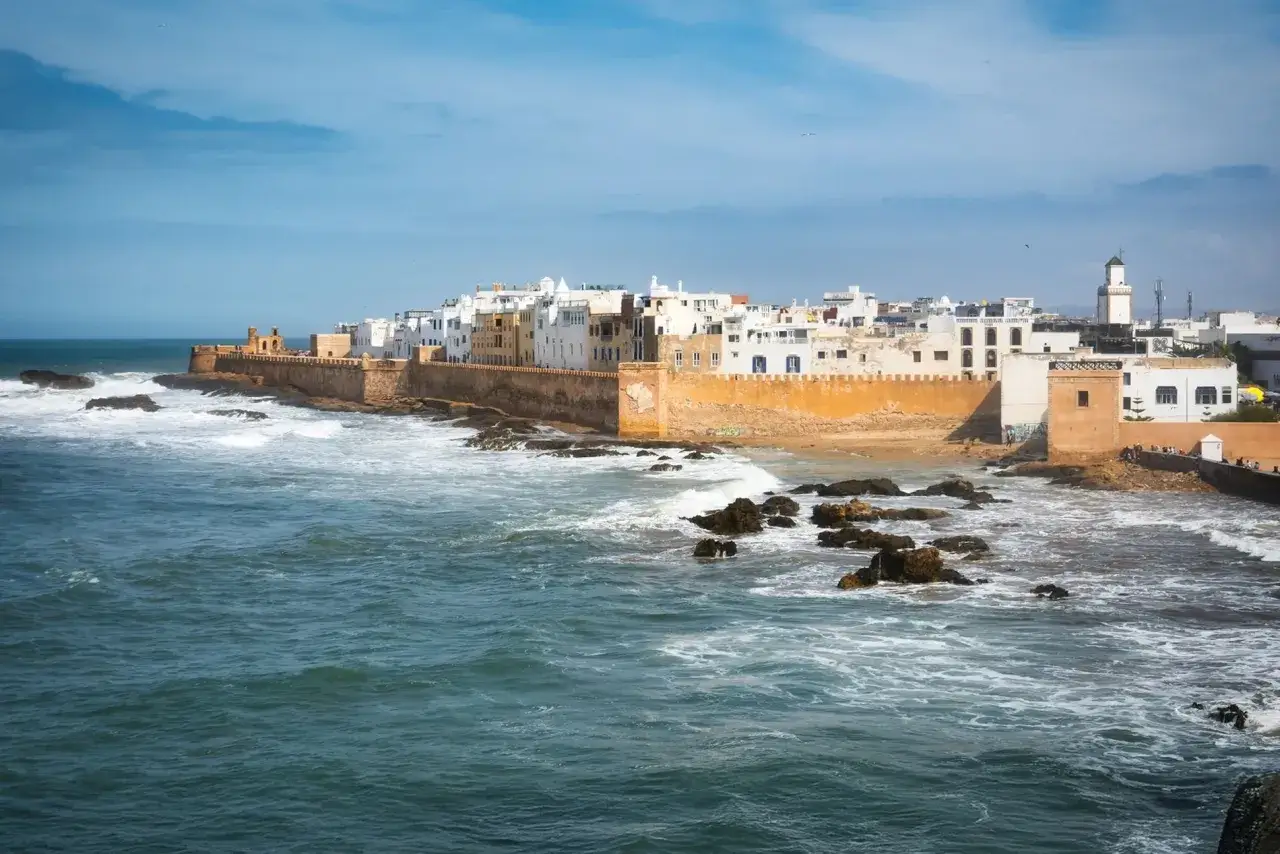 Vue de la côte d'Essaouira, avec ses remparts ocres et ses maisons blanches. La mer agitée et les rochers invitent à toutes les activités nautiques.