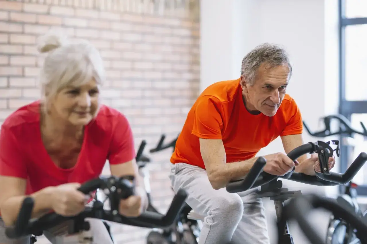 Un couple actif fait du vélo d'appartement, prouvant qu'il n'est jamais trop tard pour rester en forme, même fractionné après 60 ans.