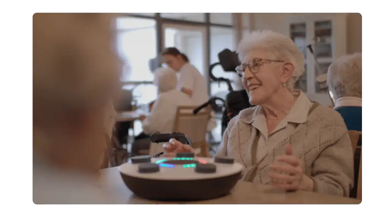 Une femme âgée rit en participant à une activité sensorielle adulte avec un appareil interactif lumineux.