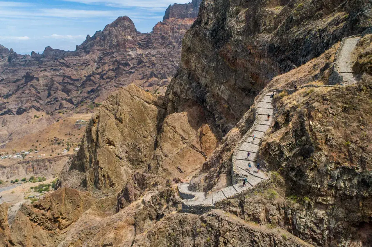 Une randonnée spectaculaire sur un sentier en pierre à flanc de montagne, avec des randonneurs profitant du paysage aride du Cap Vert.