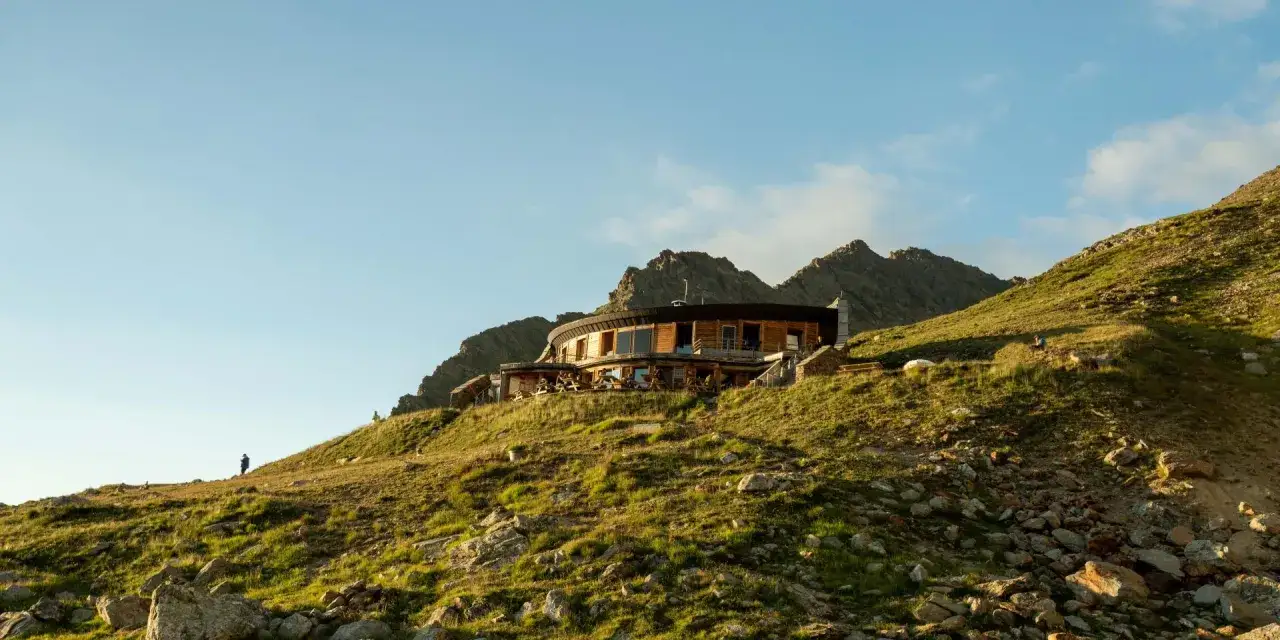 Un refuge moderne sur une crête rocheuse, offrant une vue imprenable. Un randonneur solitaire admire le paysage, prêt pour le refuge tour du mont blanc.