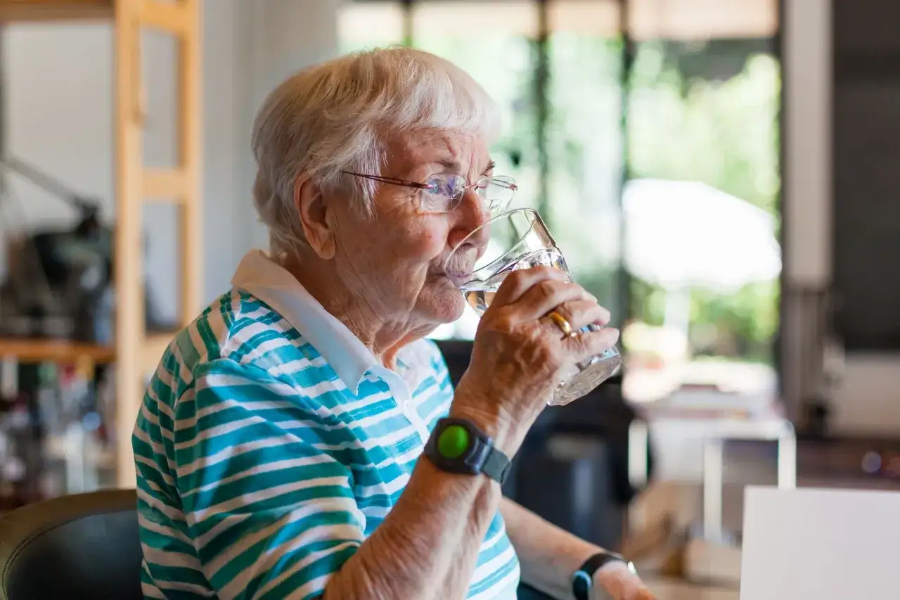 Une femme âgée boit un verre d'eau, assurant son hydratation optimale.