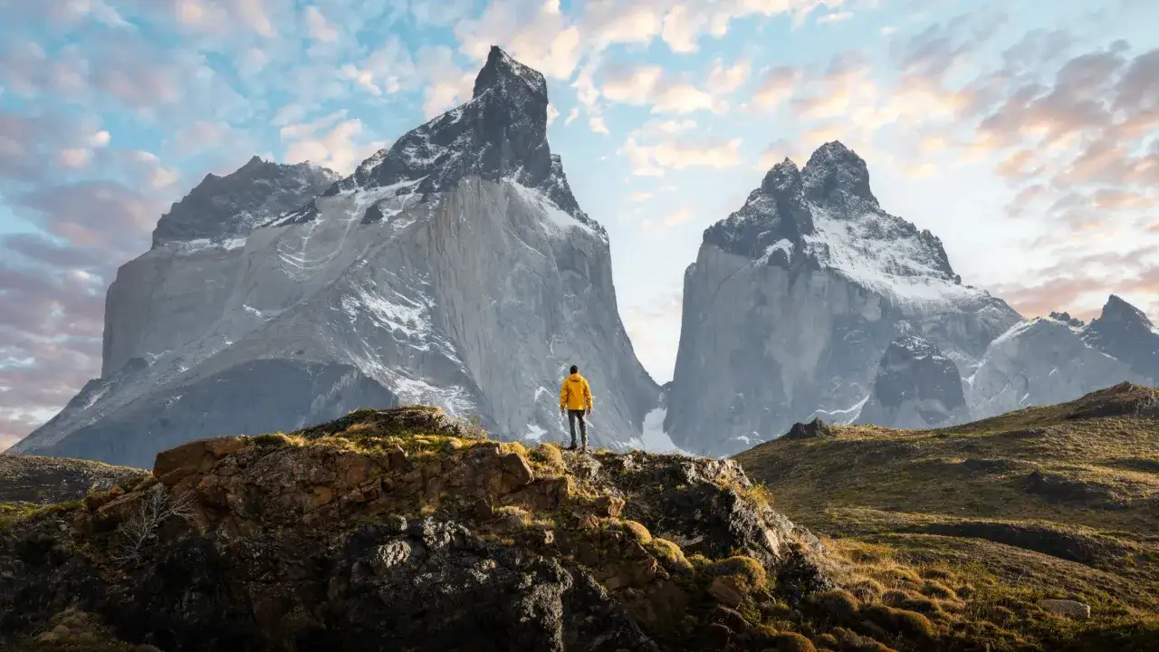Un randonneur en jaune admire les pics majestueux lors d'une randonnée argentine. Le ciel est parsemé de nuages roses et bleus.