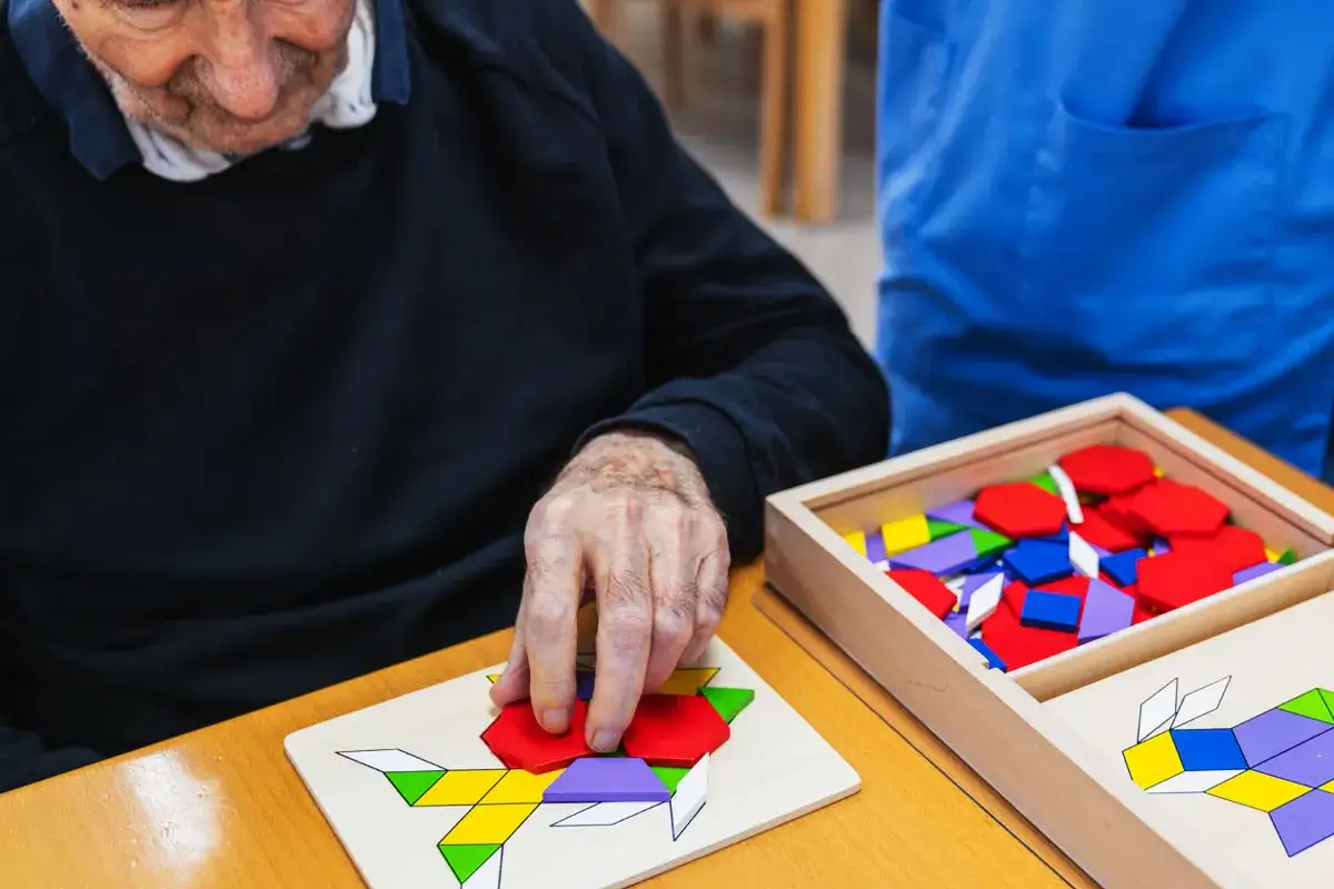 Un homme âgé manipule des pièces colorées pour un jeu de mémoire, une activité stimulante pour le cerveau dans le cadre d'un jeu Alzheimer.