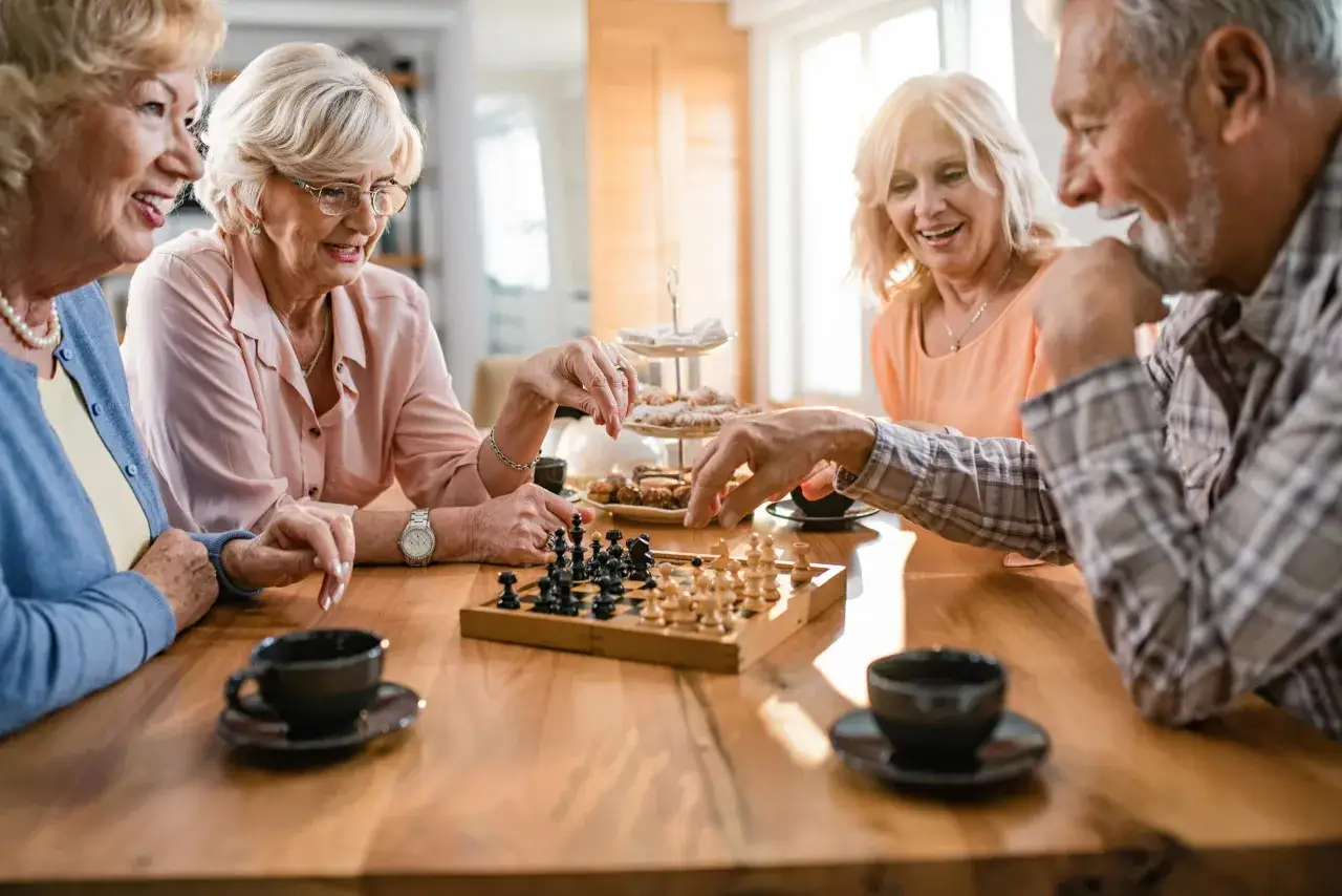 Quatre amis profitent d'un jeu d'échecs, un excellent exercice de mémorisation, autour d'une table en bois avec des tasses de café et des biscuits.