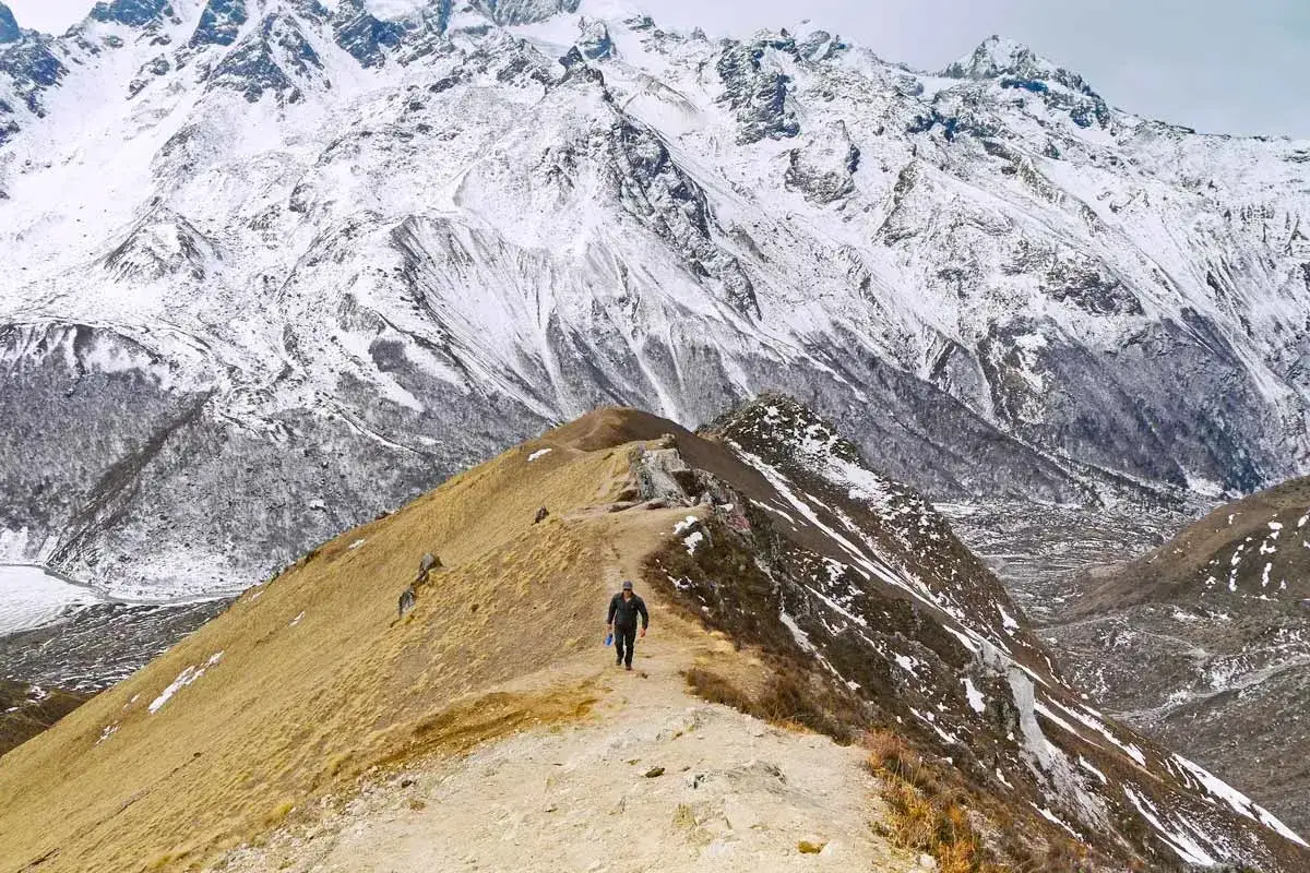 Un randonneur solitaire sur un sentier étroit, dominant une vallée enneigée. Un paysage spectaculaire du Langtang Trek.