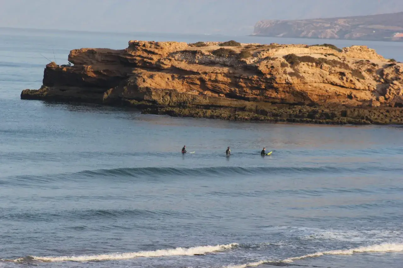 Trois surfeurs attendent la vague parfaite près des falaises de Tamraght.