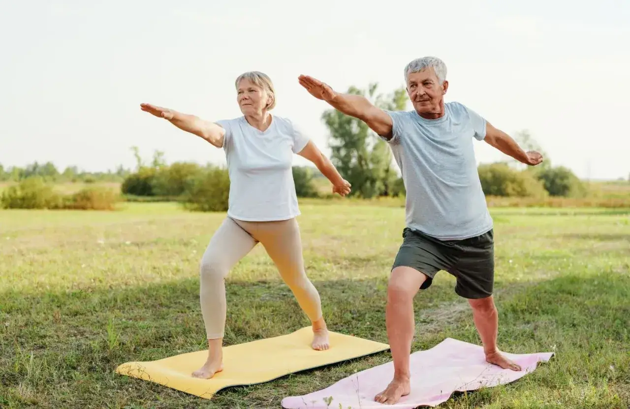 Couple âgé pratiquant le yoga en plein air, un moment de bien-être mental et physique dans la nature.