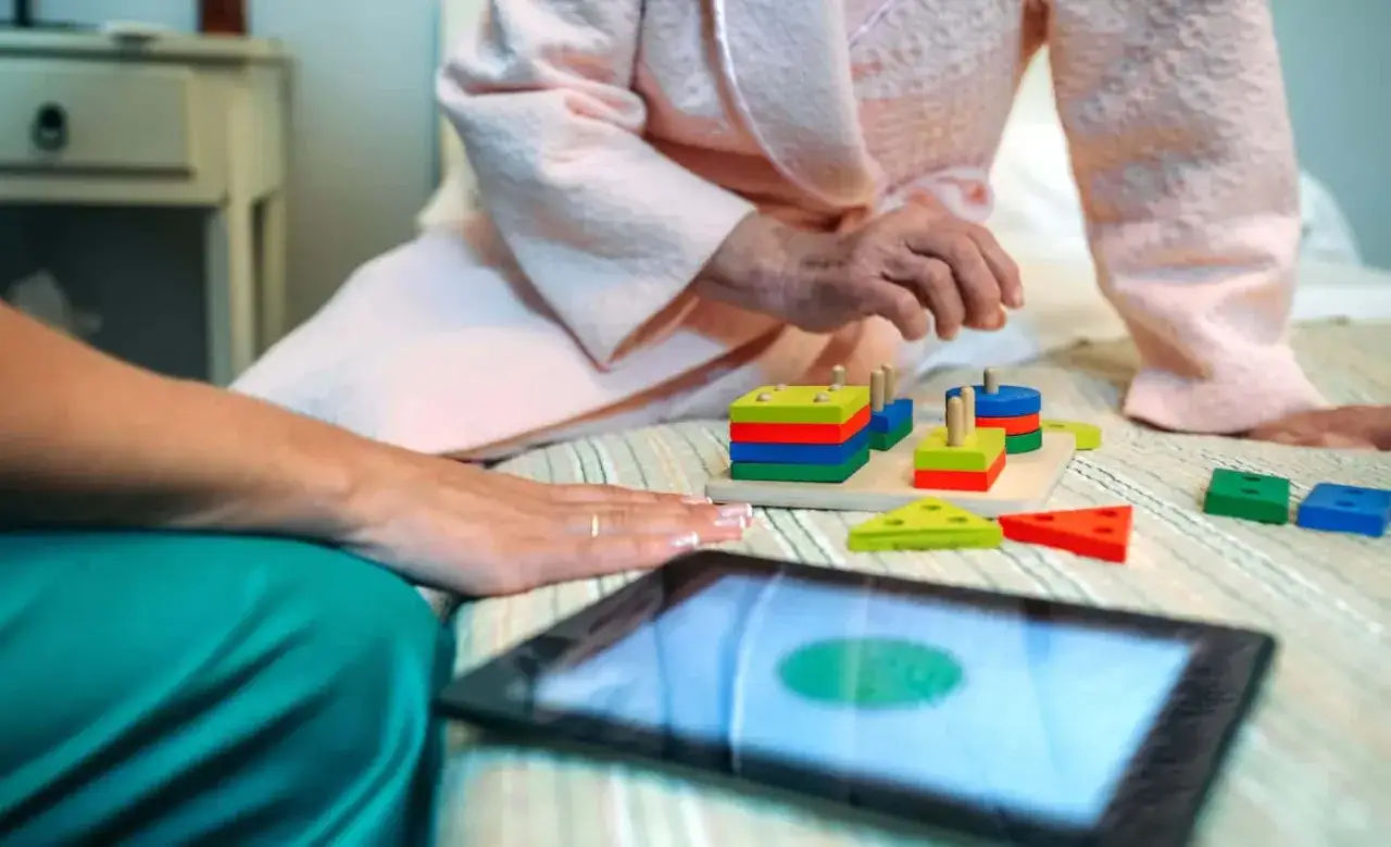 Une aide-soignante et une senior jouent avec des jeux de mémoire pour seniors gratuit, stimulant l'esprit sur une tablette.