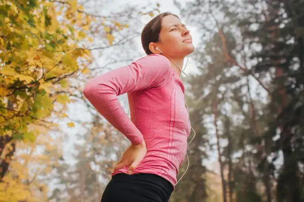 Femme en tenue de sport, le dos douloureux, se tenant la hanche. Le sport peut être mauvais pour le dos.
