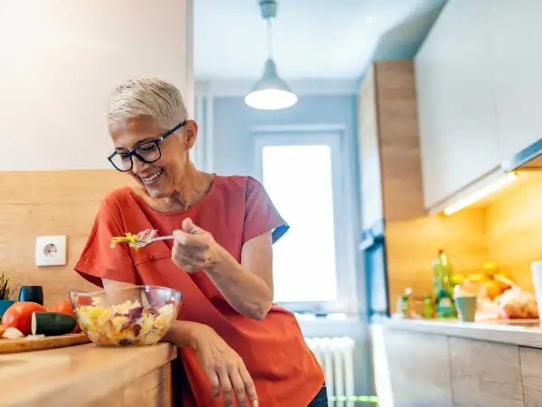 Femme souriante de 50 ans savoure une salade fraîche. Une alimentation saine pour maîtriser les calories.