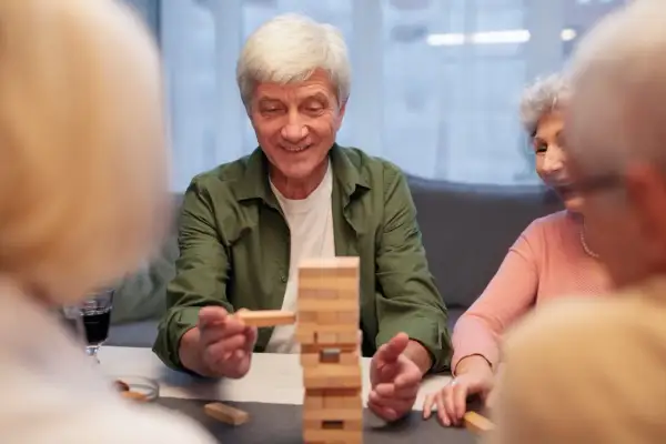 Un homme âgé sourit en retirant un bloc d'une tour Jenga. Un jeu stimulant pour la mémoire, utile dans le cadre d'un jeu Alzheimer.