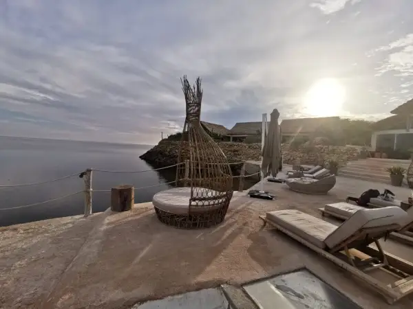 Terrasse en bord de mer à Dakhla, Maroc, avec des chaises longues, un fauteuil en rotin et des bâtiments au toit de chaume.