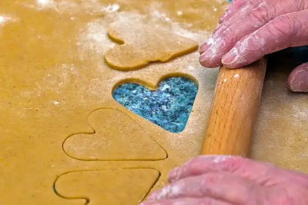 Des mains saupoudrées de farine utilisent un rouleau à pâtisserie pour découper des cœurs dans la pâte, comme des jeux de mémoire pour la Saint-Valentin.